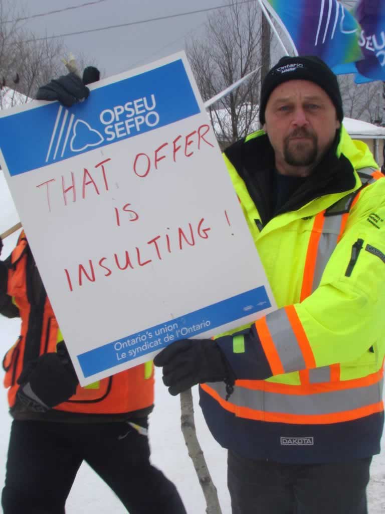 OPSEU member holds up a sign that says 'That Offer is Insulting!' in Chapleau