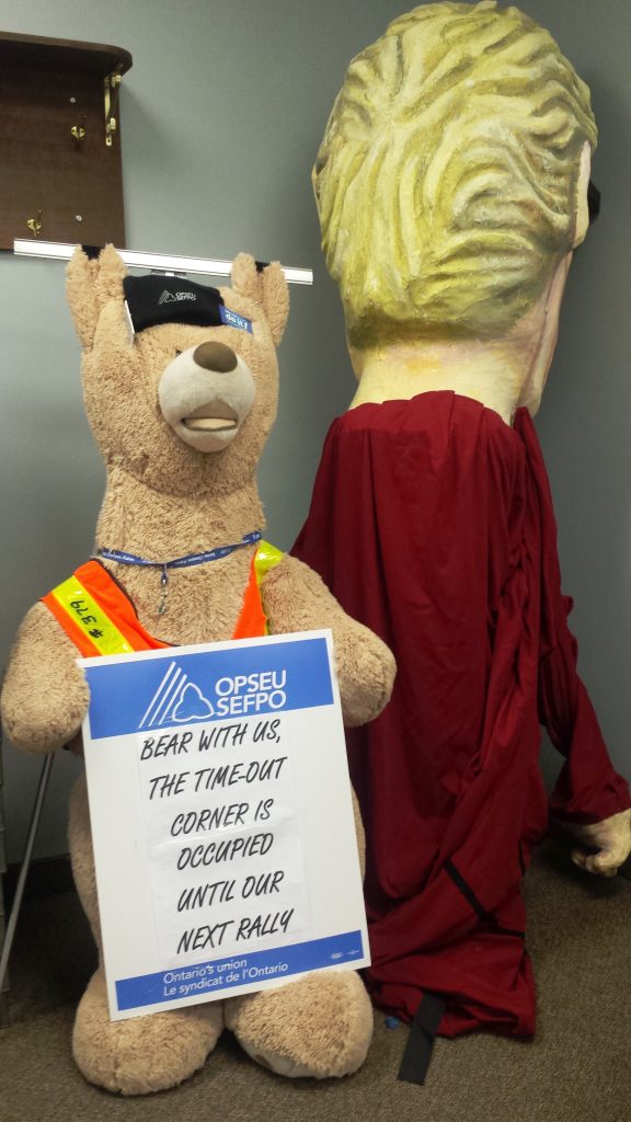 Kathleen Wynne puppet and teddy bear wearing a sign that says 'Bear with us, the time out corner is occupied until our next rally'
