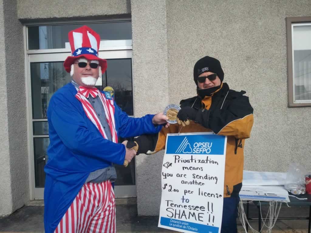 OPSEU member dressed as Uncle Sam shaking someone's hand. Man wearing sign about privatization