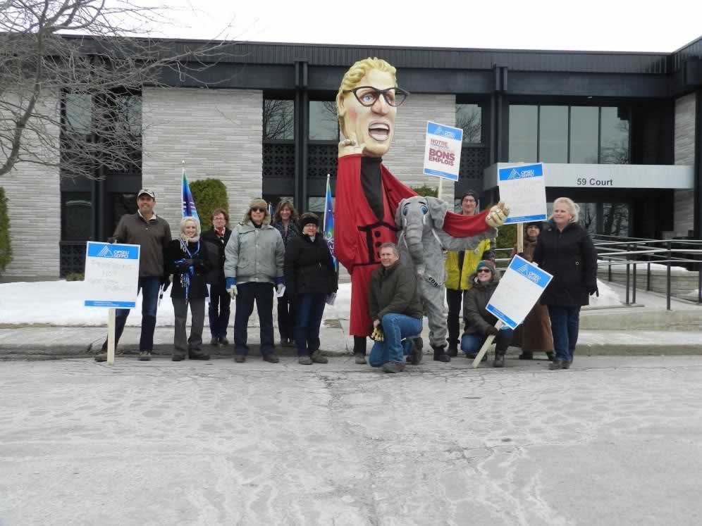 OPSEU members at rally, holding picket signs & next to Kathleen Wynne puppet