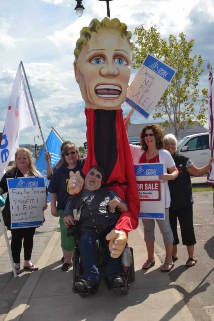 OPSEU members posing next to Kathleen Wynne puppet and holding signs that say: Ontario - not for sale