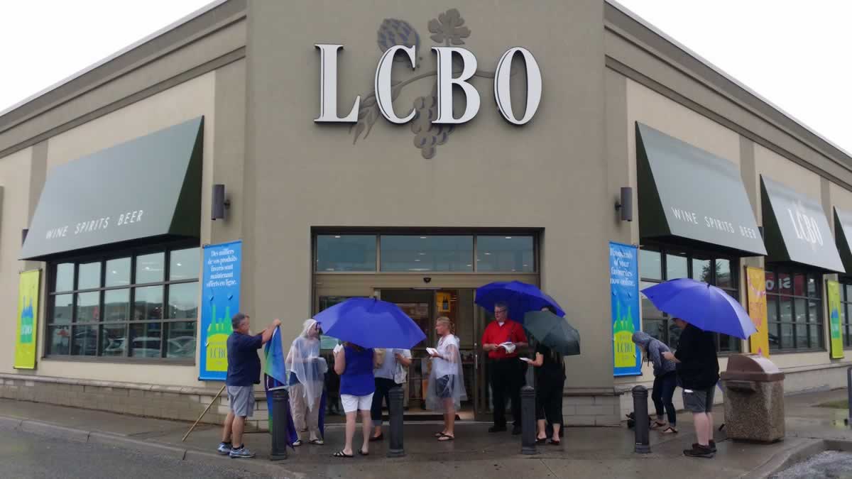 People standing outside an LCBO with umbrellas for protest