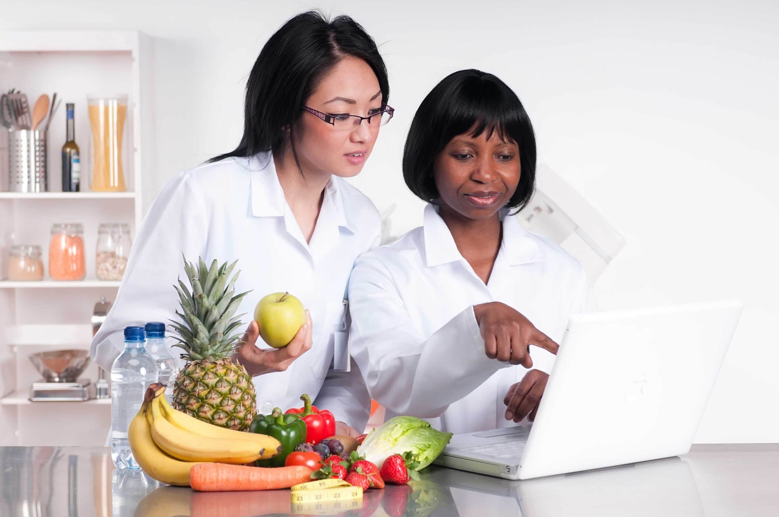 Dietitians discussing some information on a laptop with a pile of fruit and vegetables next to them.