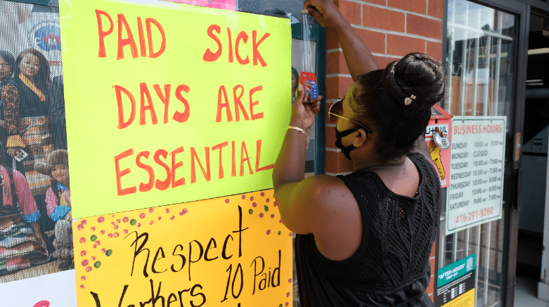Woman puts up sign saying Paid Sick Days are Essential