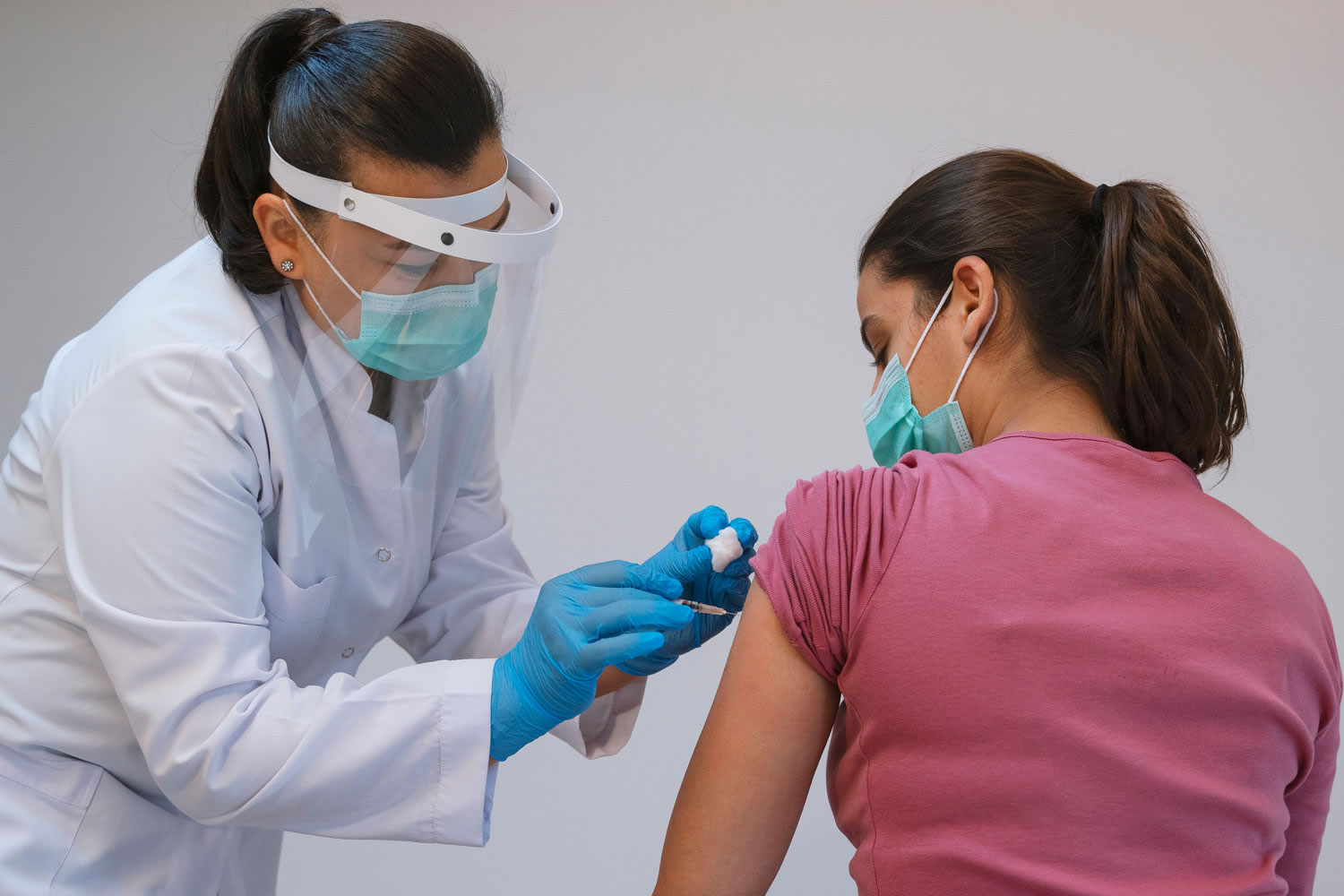 Health care worker wearing mask, face shield and gloves administers vaccine for a woman