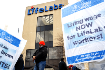 Striking LifeLabs workers in front of a building with a LifeLabs sign