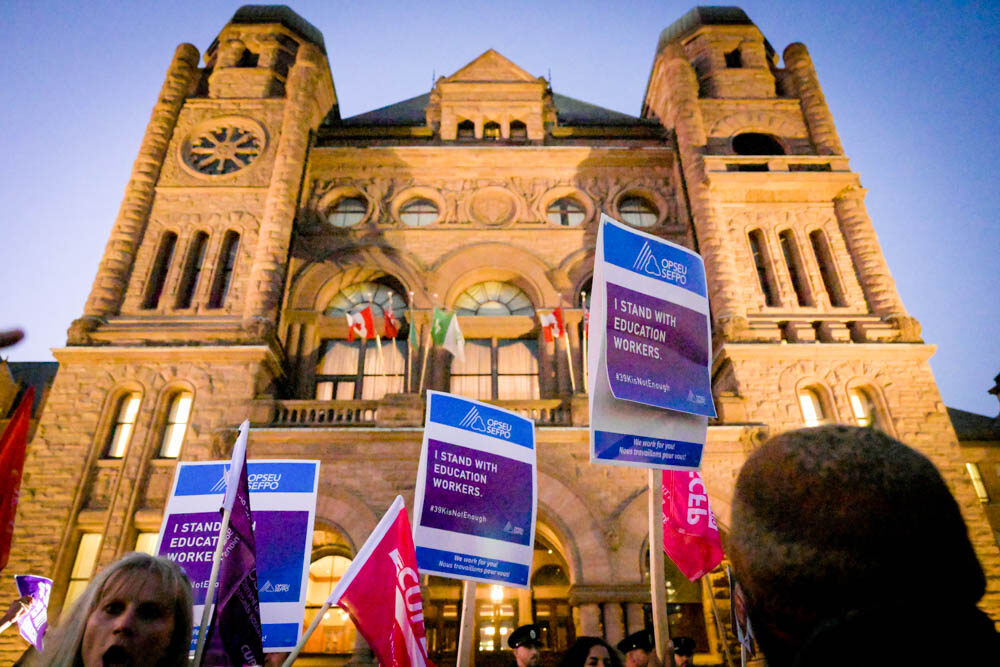 Many OPSEU/SEFPO picket signs in front of Queen's Park in the evening.