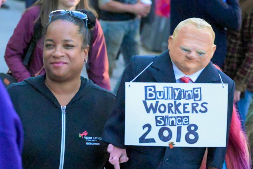 A worker at a rally by a bust of Doug Ford that reads 'Bullying Workers Since 2018"