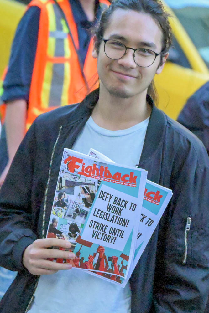 A worker at a rally holding a magazine called "Fightback".