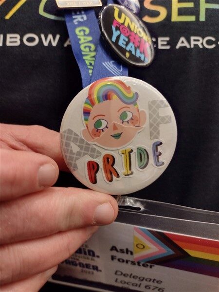 Close-up of button that says "AF Pride" with a cartoon face with rainbow-striped hair