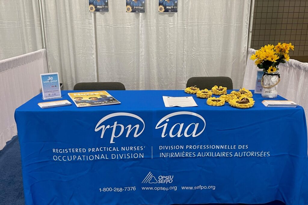 Convention marketplace table, blue tablecloth that has RPN IAA logos, sunflowers and posters on the table.