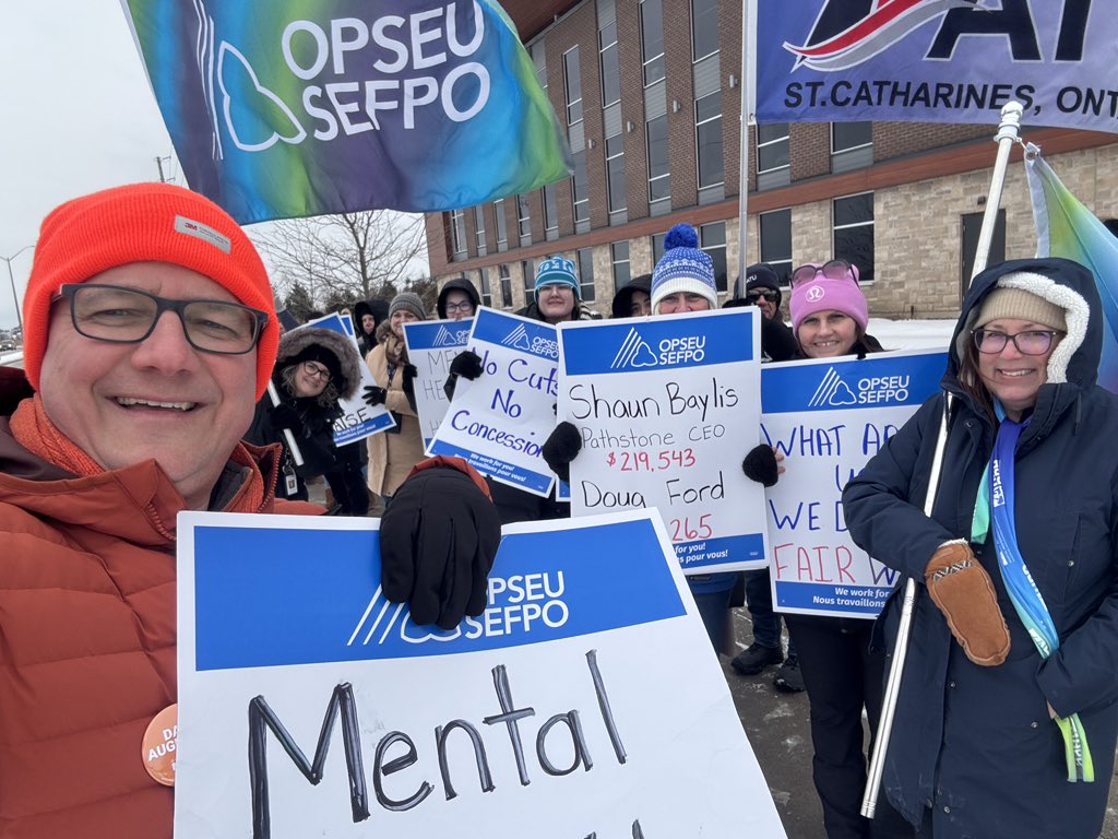 Group of people standing together holding picket signs and OPSEU/SEFPO flag outside the Branscombe Centre