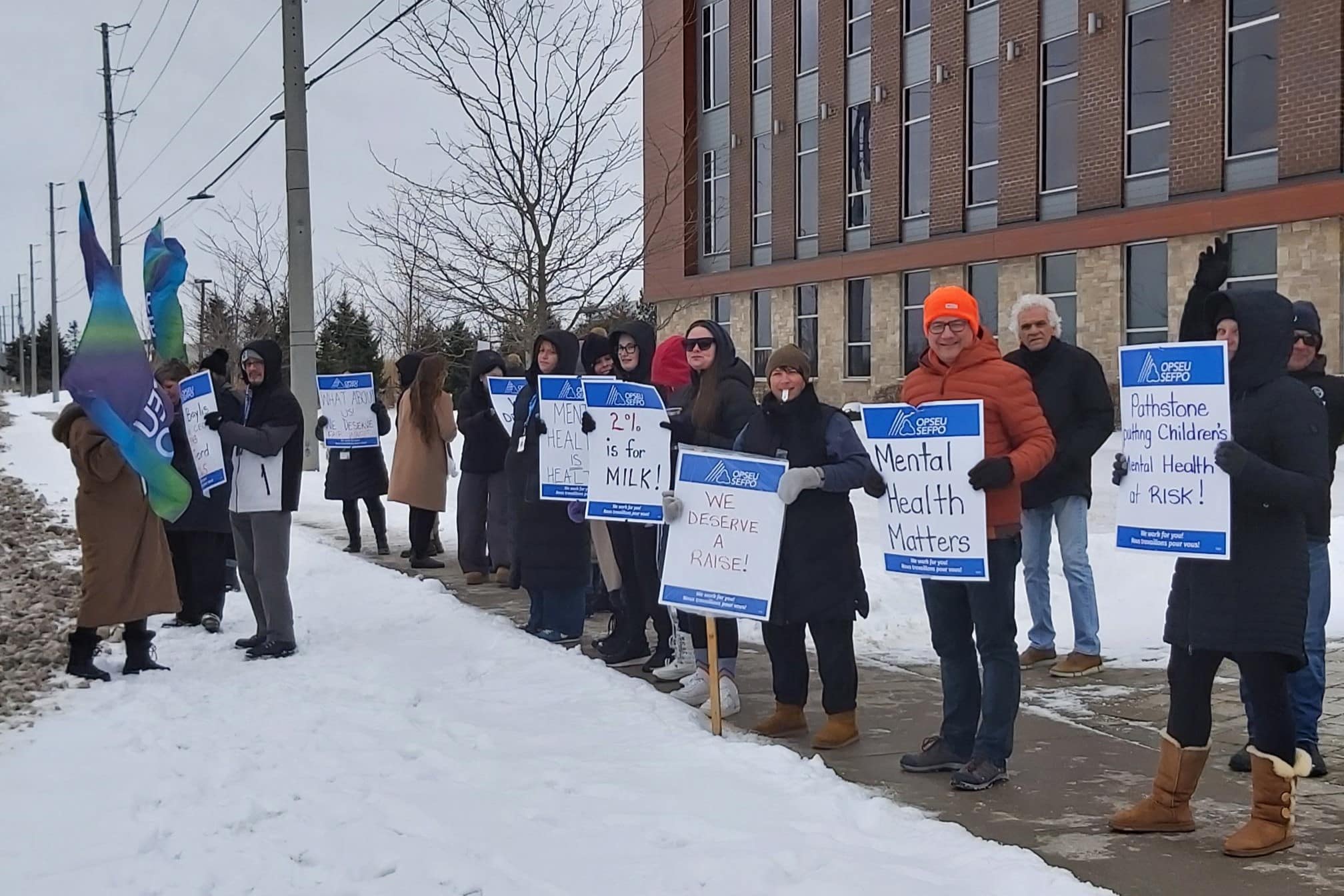 A group of people stand in a line holding picket signs in front of Branscombe Centre.