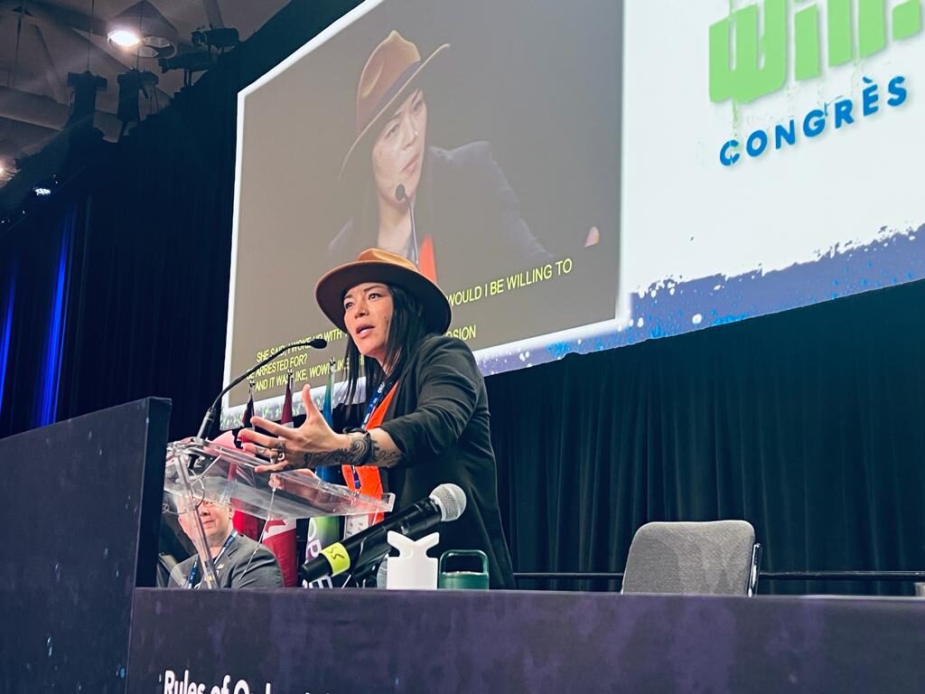 Layla Staats addresses convention with her image projected on large screen behind her