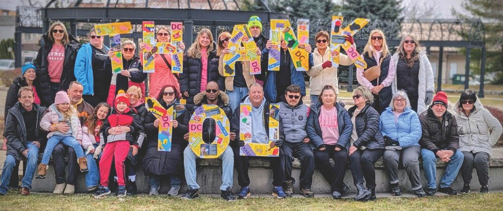 A group of roughly two dozen people smiling and holding signs that read "Thank you"