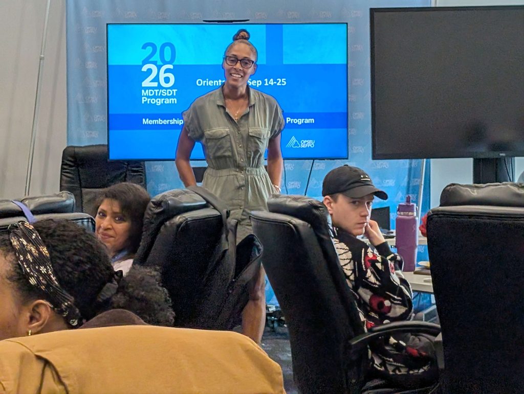 Equity Vice President Dr. Crystal Garvey stands at the head table addressing several participants seated in chairs. The screen behind Dr. Garvey says "2026 MDT/SDT Program"