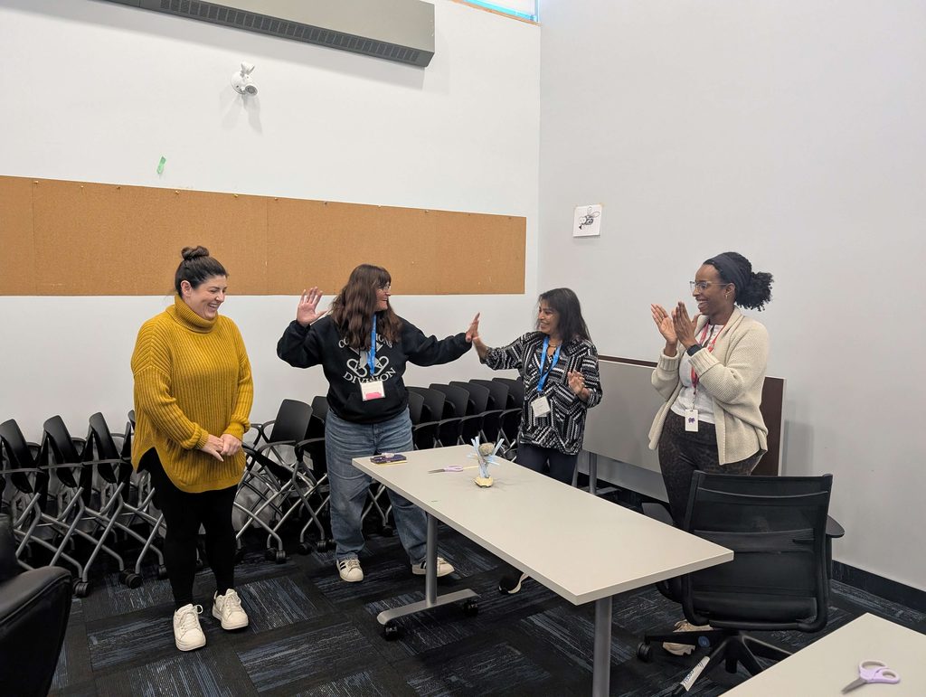 Four participants are standing behind a table holding a rock sculpture. Two people high five while another person claps.