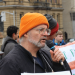 Matthew Behrens speaking into a mic during a rally