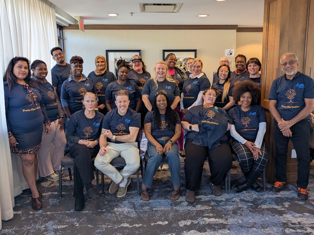 Group picture of people posing together, wearing dark blue shirts that say "Train the Trainer" on them."