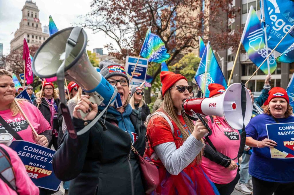 Two people, both holding megaphones, march in a crowd of protesters with OPSEU/SEFPO signs and flags.