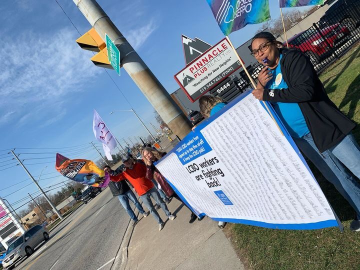 Crowd of people standing together with OPSEU/SEFPO and other union flags, and a large banner with thousands of signatures of LCBO workers